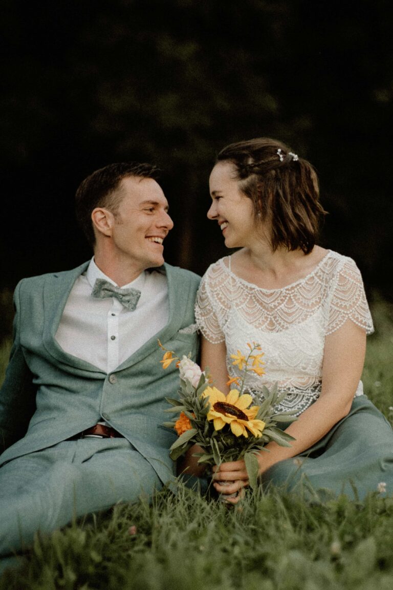couple sitting in grass smiling with flowers in analog look